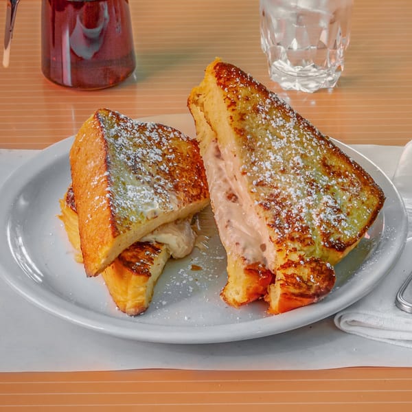 Golden-brown French toast stuffed with cream cheese, dusted with powdered sugar, on a white plate.