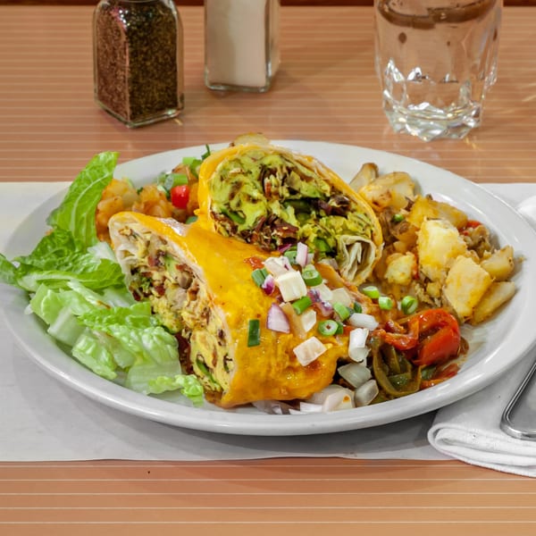 A breakfast burrito with cheese, avocado, and salsa, served with home fries and lettuce.
