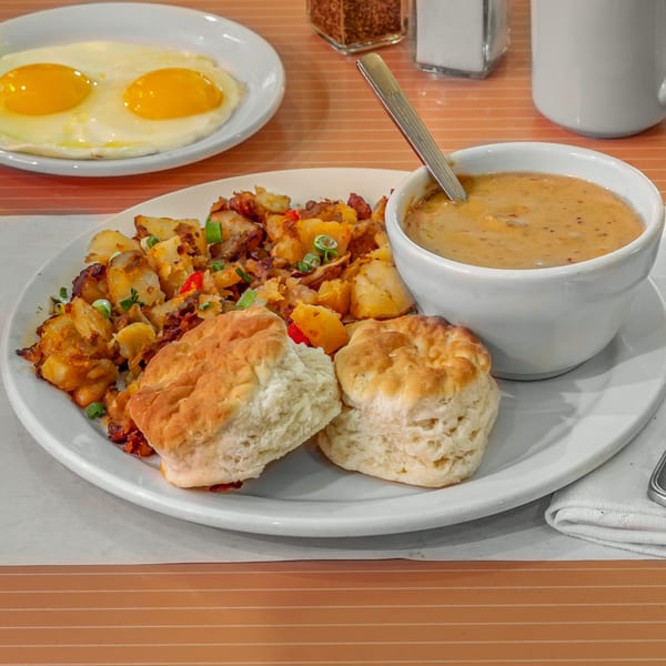 A Breakfast Club and Grill breakfast plate with biscuits, gravy, home fries, and fried eggs.