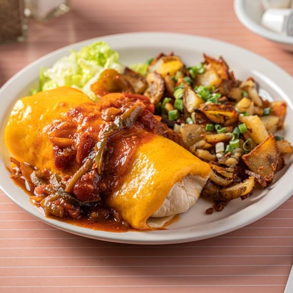 A breakfast burrito smothered in cheese and salsa, served with crispy home fries and lettuce.