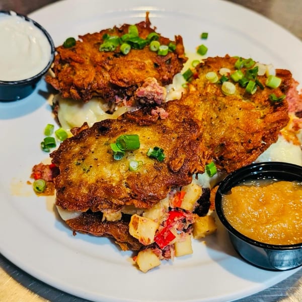 Three golden-brown potato pancakes topped with green onions, served with applesauce and sour cream.